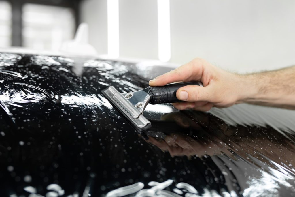 Car window tinting installer smoothing tint film on rear glass.