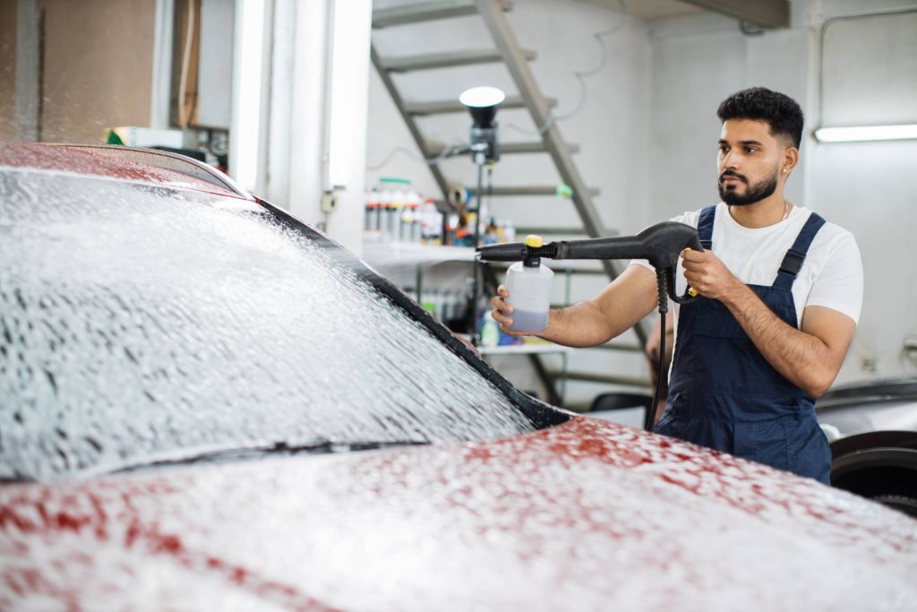 Professional hand car wash applying foam spray to vehicle exterior for safe cleaning.